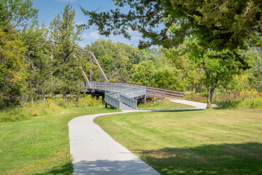 A few of the park with N wheelchair accessible ramp leading to a trail on a bridge over a river