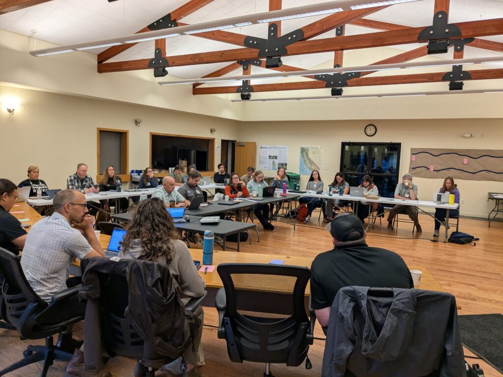 A large group of people gather around tables for a meeting