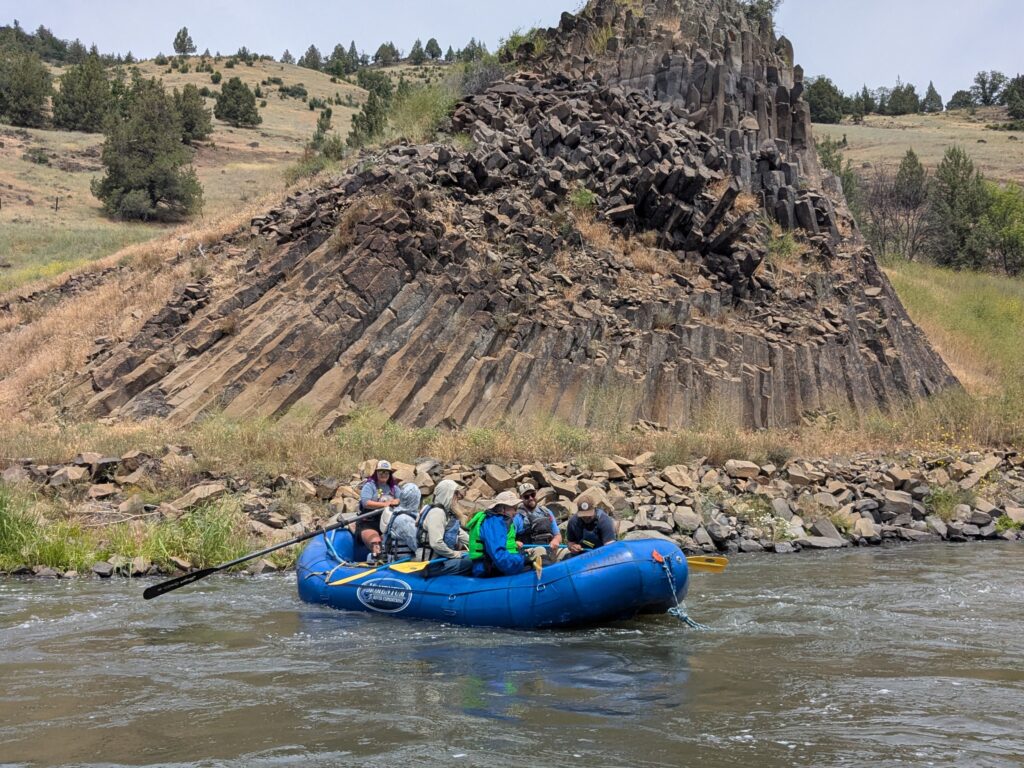 A river raft floats beside a formation of columnar basalt on the Klamath River