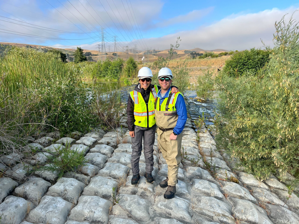 Two people in hard hats and high visibility vests stand on a concrete erosion control mat